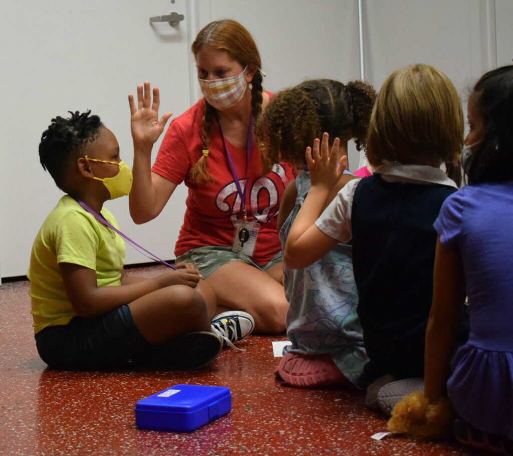 Kelly sits in floor with four young acting students in a classroom with a red floor.